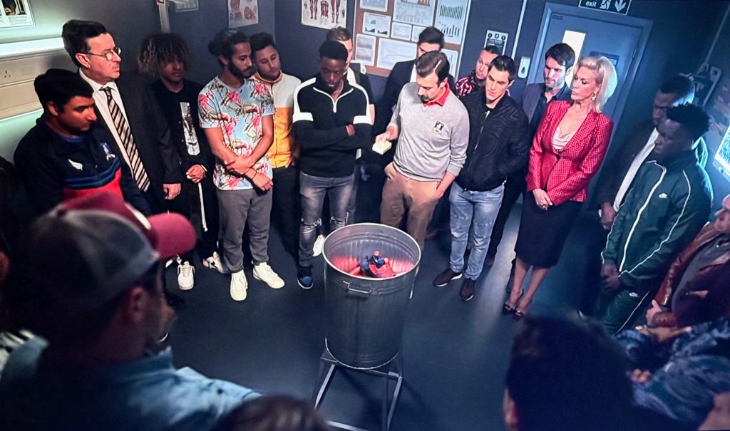The football team stand inside the treatment room, huddled around a flame in a metal trash bin